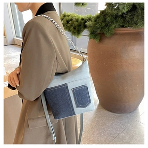 Detail of denim patchwork crossbody bag with metal chain strap and side pocket design