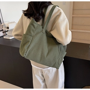 Dark green corduroy tote bag showing spacious interior and side pocket on a model