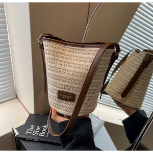 Close-up of woven straw bucket bag with brown leather trim and metallic brand plaque