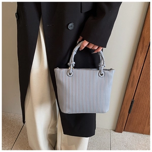 Detail of light grey pleated bucket bag featuring vertical accordion folds and woven handle