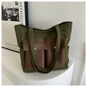 Detail of dark green canvas tote bag with brown faux leather pockets and metal buckles