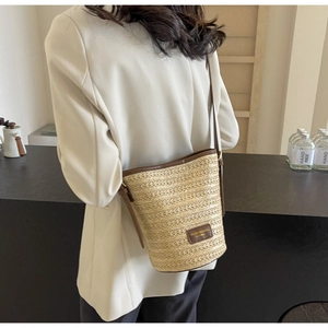 Close-up of woven straw bucket bag with dark brown leather strap and brand label detail