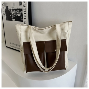 Detail of canvas tote bag with contrast brown leather front pockets and metal snaps