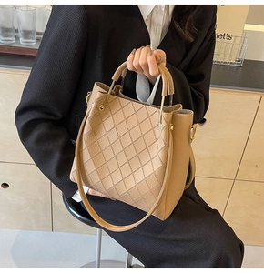 Detail view of beige quilted bucket bag with circular handles and leather texture
