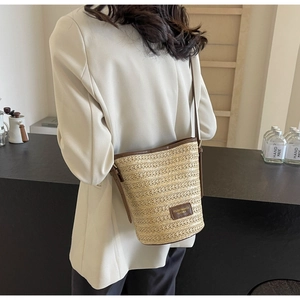 Detail of woven straw bucket bag with leather logo patch and adjustable crossbody strap
