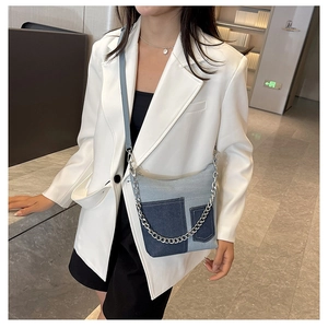 Detail of patchwork denim shoulder bag with silver chain strap on a white blazer