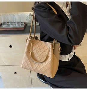 Close-up of khaki quilted bucket bag with gold U-shaped handle and textured leather