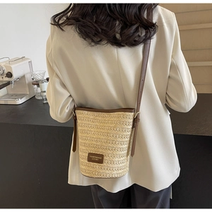 Detail of hand-woven straw bucket bag with brown leather strap worn by a female model