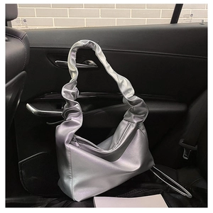 Detail of silver pleated cloud baguette bag with glossy metallic finish in car interior