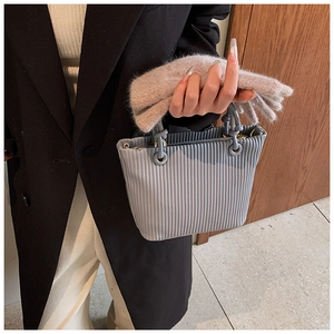 Close-up of a grey pleated bucket bag with vertical textures and gold metal hardware