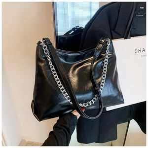 Detail of glossy wrinkled leather texture and silver chain on a black tote bag