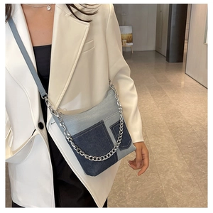 Detail of blue patchwork denim bucket bag with silver chain strap on white blazer