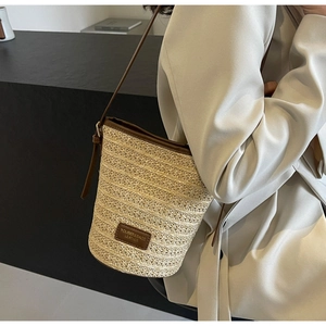 Detail of woven straw bucket bag showing brown leather trim and brand logo patch