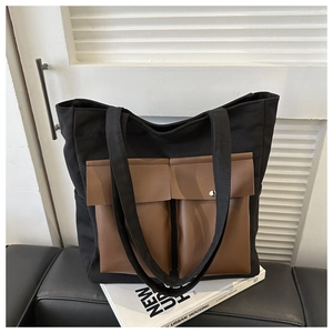 Detail view of black canvas tote bag featuring dual brown leather pockets with silver snaps