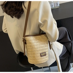 Close-up of woven straw bucket bag with brown leather trim and adjustable shoulder strap
