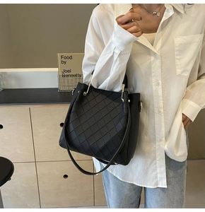 Detail of black quilted leather bucket bag with gold hardware and woven handle