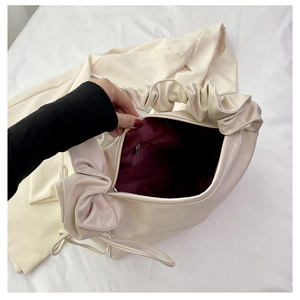 Detail of soft cream croissant bag featuring pleated cloud handle and burgundy fabric lining