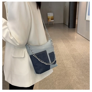 Detail of a patchwork denim bucket bag with silver chain strap shown on a model