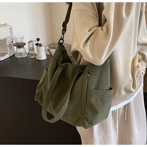 Detailed side view of an olive green corduroy tote bag worn by a model in a cafe