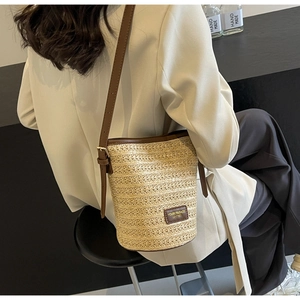 Detail of hand-woven straw bucket bag with brown leather trim and adjustable strap