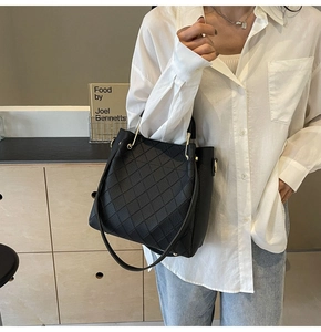 Detail of black quilted leather bucket bag with metallic handles and a detachable strap