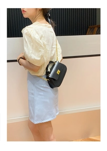 Detail view of black leather handbag with a golden square lock and metal chain strap