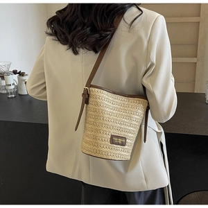 Close-up of the woven straw bucket bag with brown leather strap and brand label