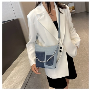 Detail of blue denim patchwork shoulder bag featuring silver chain and pocket accents