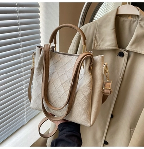 Detail of white bucket bag featuring diamond lattice texture and brown leather strap