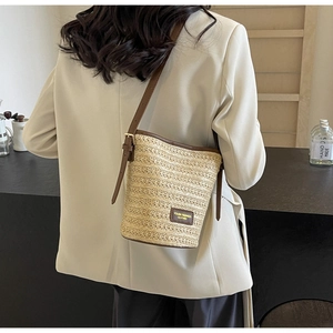 Detail of woven straw bucket bag with adjustable brown leather strap and metal buckle