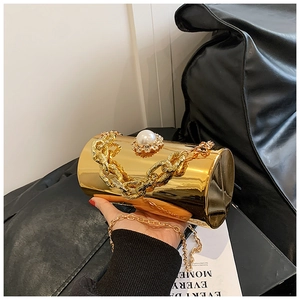 Detail of golden cylinder bag with large pearl closure and twist chain strap