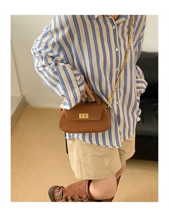 Brown leather crossbody bag with gold twist lock and chain strap on a striped shirt