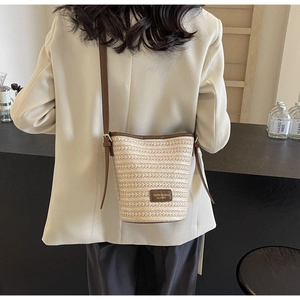 Detail of woven straw bucket bag with leather strap worn cross-body by a model