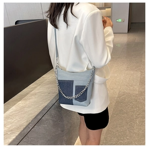 Detail of patchwork denim bucket bag with silver chains worn over a white blazer