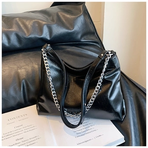 Detail of minimalist black glossy leather shoulder bag with bold silver chain and strap