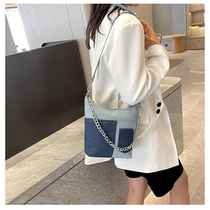 Detail of denim patchwork bucket bag with silver metal chain on shoulder