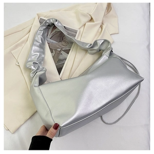 Close-up of shiny silver baguette bag featuring a wide pleated shoulder strap detail
