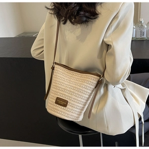 Detail of hand-woven straw bucket bag with adjustable leather strap and brand logo patch