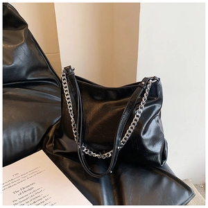 Detailed view of black wrinkled leather tote with silver chain straps on a leather seat