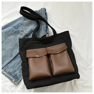 Detail of black canvas tote bag with brown leather pockets and silver metal buttons