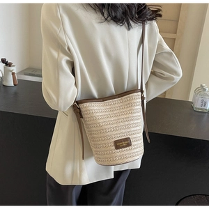 Detailed close-up of woven bucket bag with brown leather trim and elegant shoulder strap