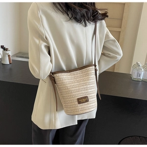 Detail of hand-woven beige straw bucket bag featuring a premium brown leather logo patch