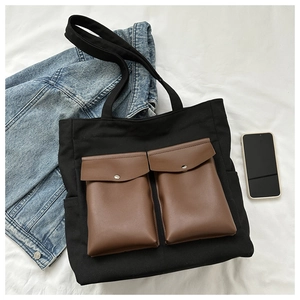 Close-up of black canvas tote bag with brown front pockets and silver snap buttons