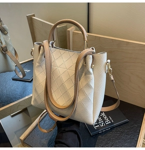 Detail of cream leather bucket bag with diamond stitching and khaki handle on wood background