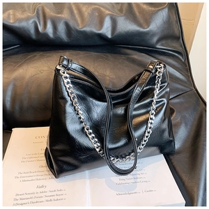 Detail of glossy black leather tote bag with silver chain and subtle texture on a magazine