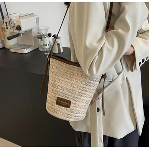 Close-up of woven straw bucket bag with premium leather trim and brand label detail