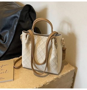 Detail of lychee pattern cream leather bucket bag with brown woven handle and gold hardware