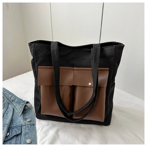 Detail of canvas tote bag showing dark brown leather front pockets and metal buckle design