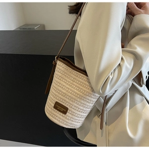 Detailed close-up of woven beige straw bucket bag with premium brown leather trim