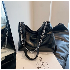 Detail of glossy black pleated leather bag with a bold silver metal chain strap